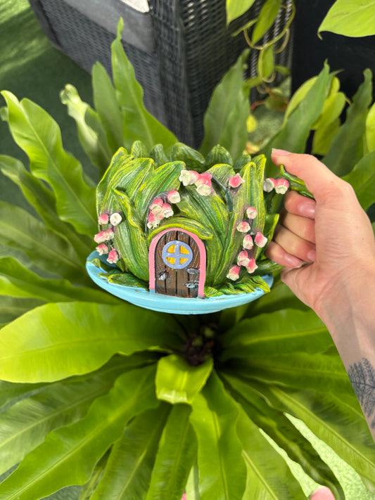 Decorative fairy home planter held by a hand against a green leafy background