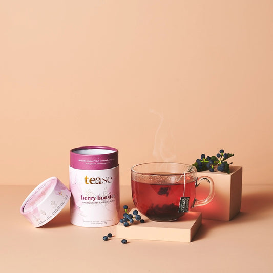 Tea canister labeled 'tease' with a glass of steaming tea and berries on a beige background