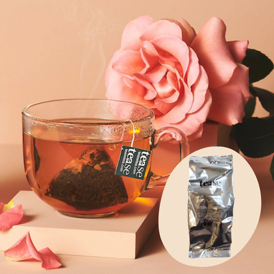 Glass of tea with a teabag labeled 'tease' next to a pink rose on a beige background.