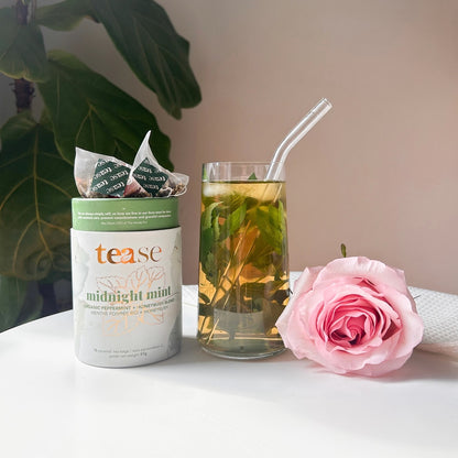 Tea packaging with a glass of tea and a pink rose on a white surface.