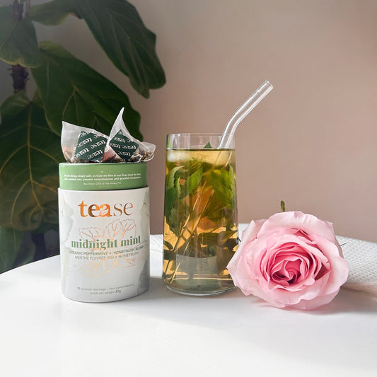 Tea packaging with a glass of tea and a pink rose on a white surface.