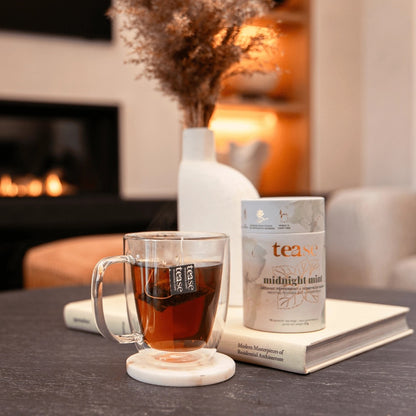 Tea cup with a package of 'tease' tea on a table in a cozy room with a fireplace.