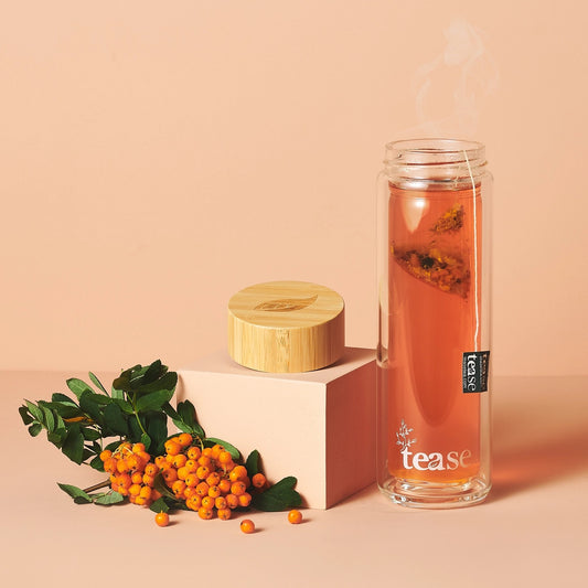 Tease Glass bottle of tea with a wooden lid and berries on a beige background