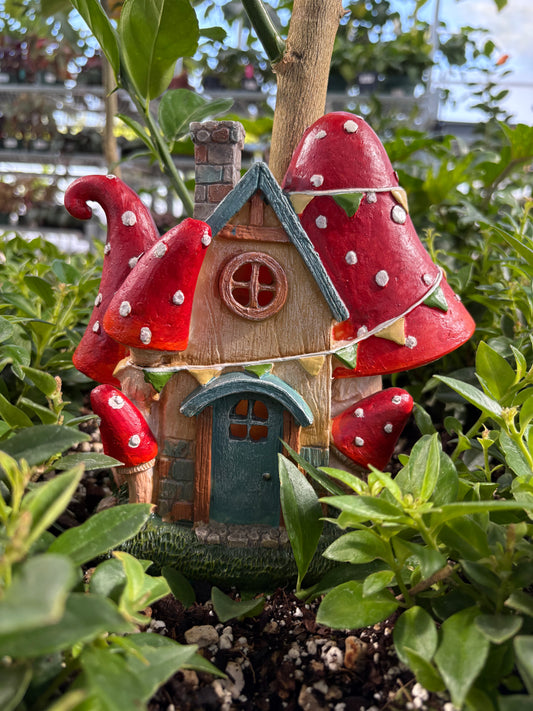 Decorative fairy house with red mushroom caps surrounded by greenery