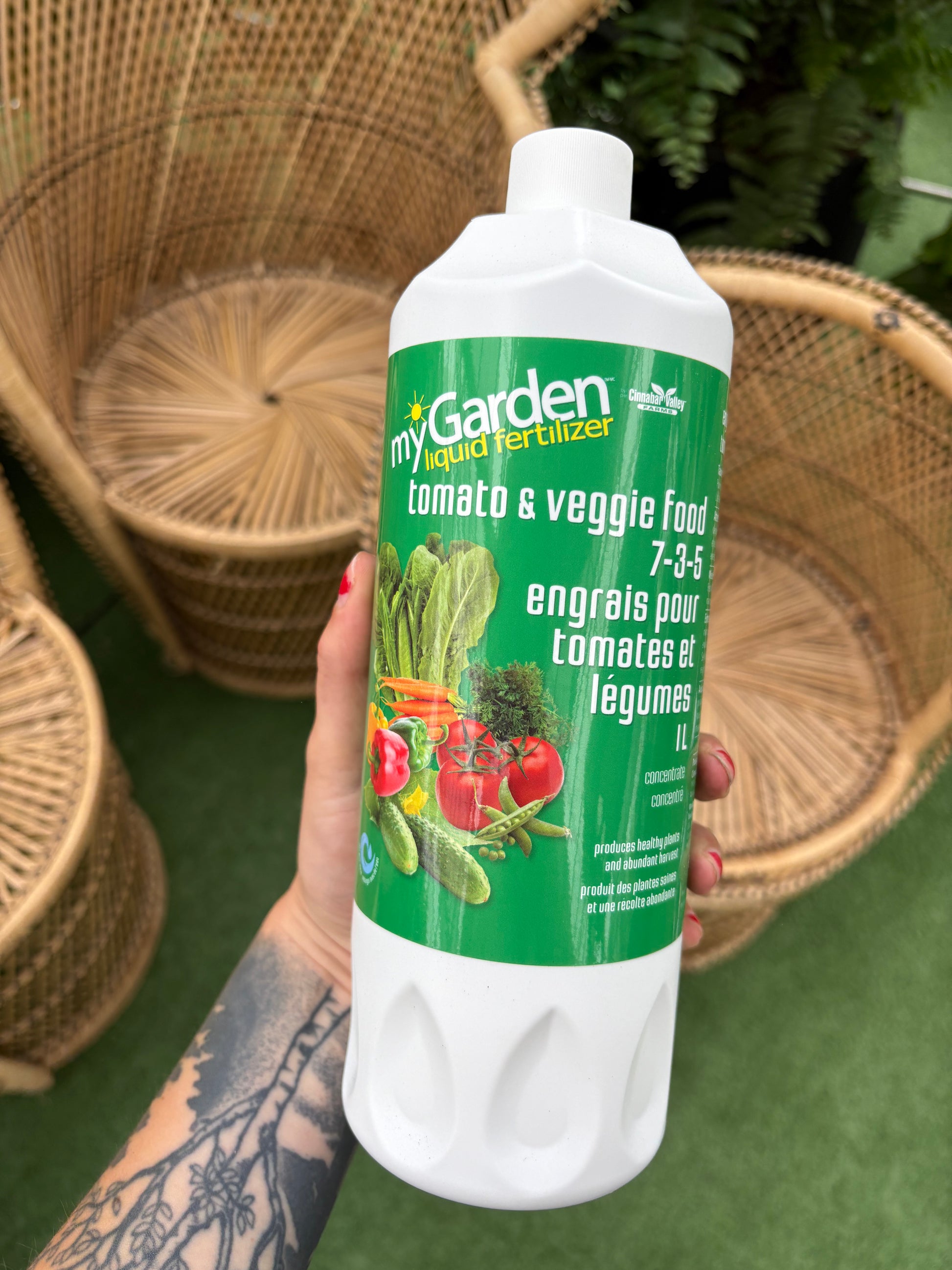 Hand holding a bottle of garden fertilizer with a green label featuring vegetables.