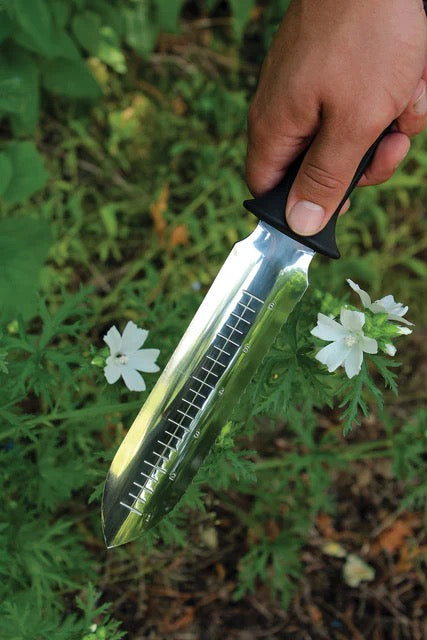 Weeding Knife Tool "Hori Hori" in someones hand going to dig it into dirt and grass with a blurred background 