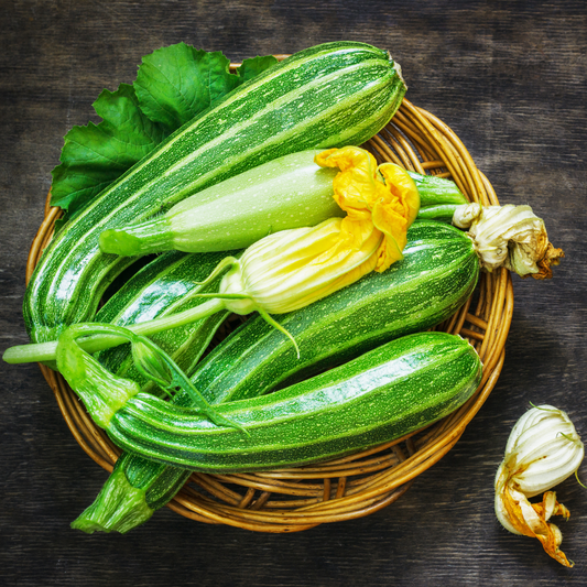 a wicker basket full of striped bright green flowering zucchini with yellow flowers against a wooden surface