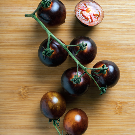 ahoy cherry tomatoes, dark red tomatoes on a vine with some loose scattered on a wooden surface