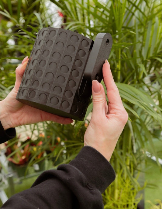 A person holding a black Algonquin Wall Mount Planter that hangs on the wall for plants.
