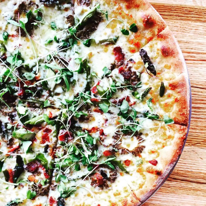 a round pizza topped with arugula micro greens resting on a wooden surface