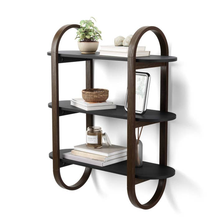 A wall-mounted shelving unit with a sleek, pill-shaped frame consisting of three tiers, with various decorative items displayed on it.