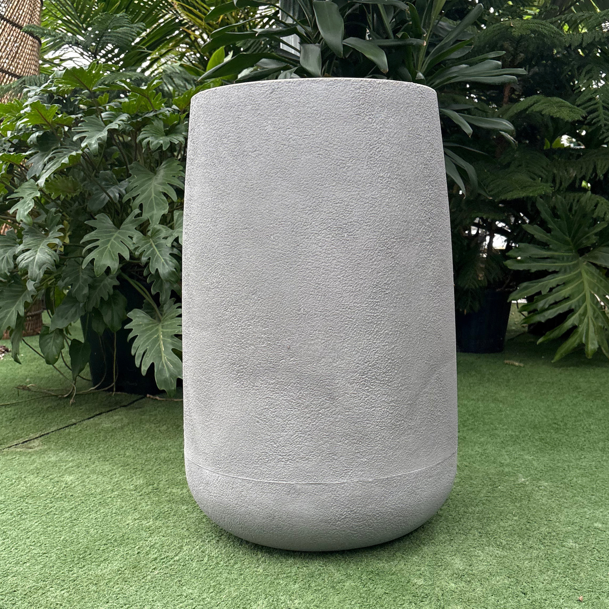 a matte grey textured finish bios round planter resting on a grass like surface in a greenhouse setting