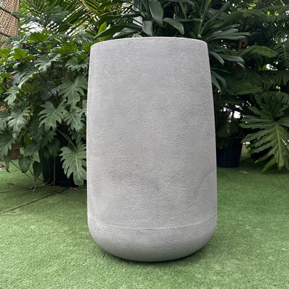 a matte grey textured finish bios round planter resting on a grass like surface in a greenhouse setting