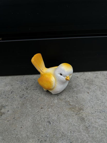 a small yellow and white ceramic bird resting on a concrete surface