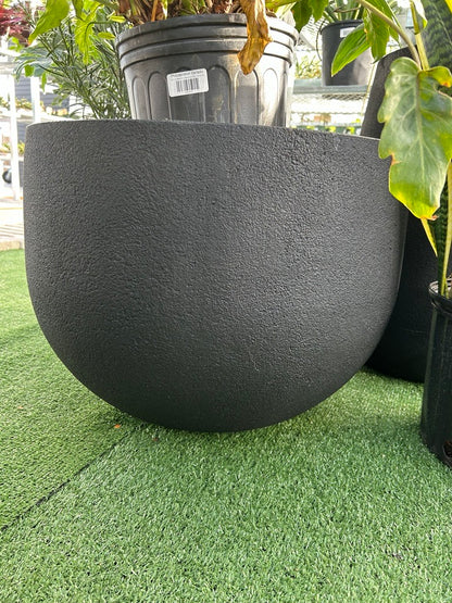 a rustic black matte planter resting on a grass like surface