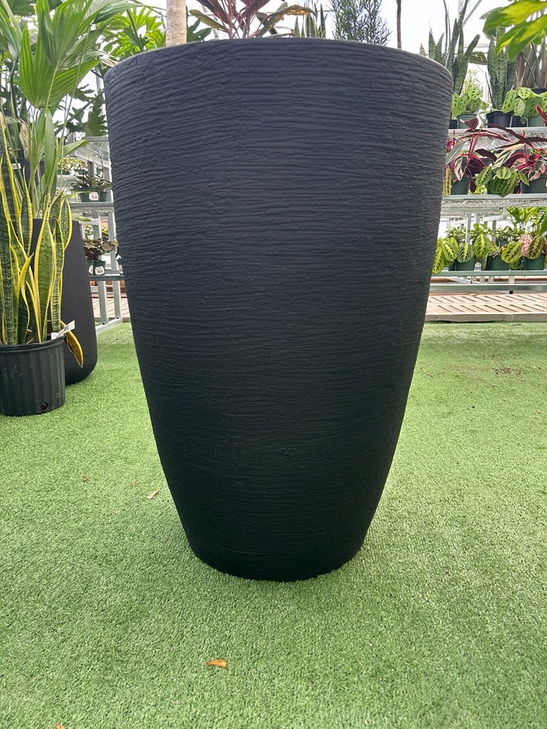 a large black planter on a grass like surface in a greenhouse setting