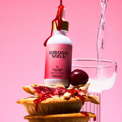 a white dropper bottle with a dark pink label that reads shroom soda black cherry with the bottle standing on multiple small cherry pies and a beverage being poured behind it with a pink background