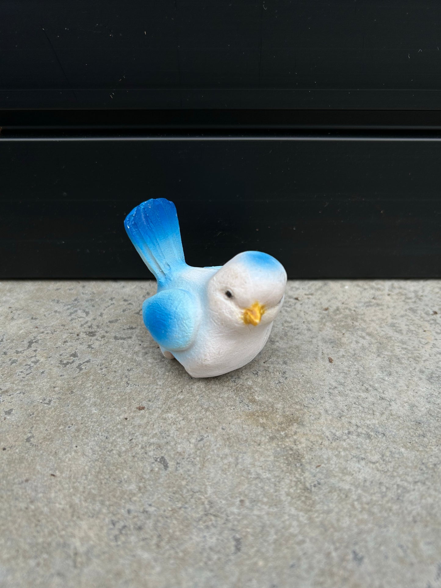 a small blue and white ceramic bird resting on a concrete surface