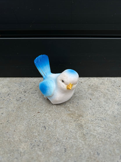a small blue and white ceramic bird resting on a concrete surface