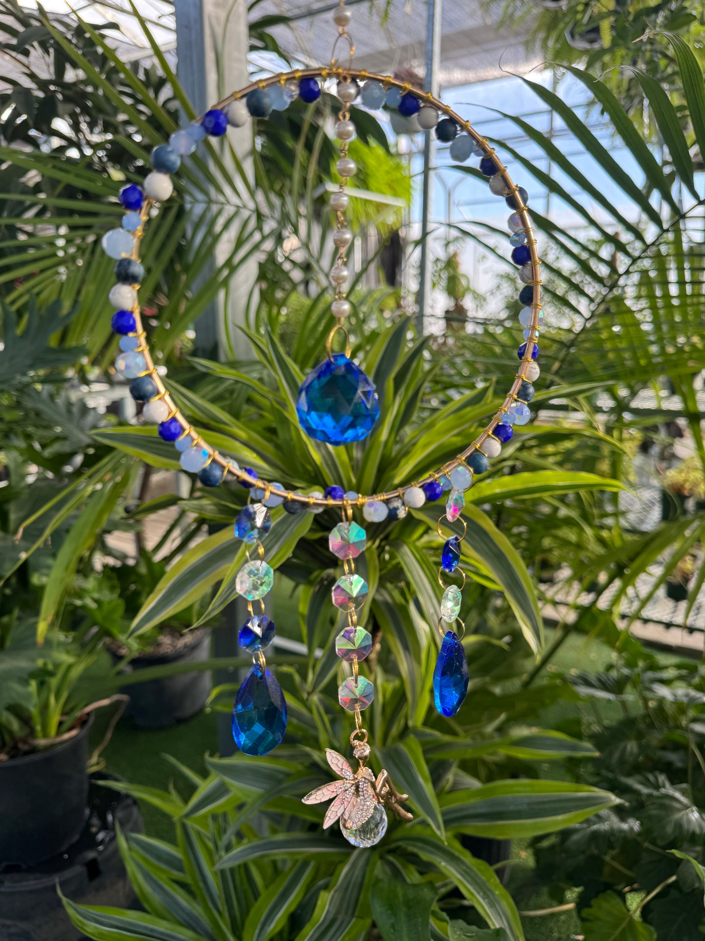 decorative round sun catcher with blue and white beading with blue and white crystals and a small golden fairy dangling from the circle