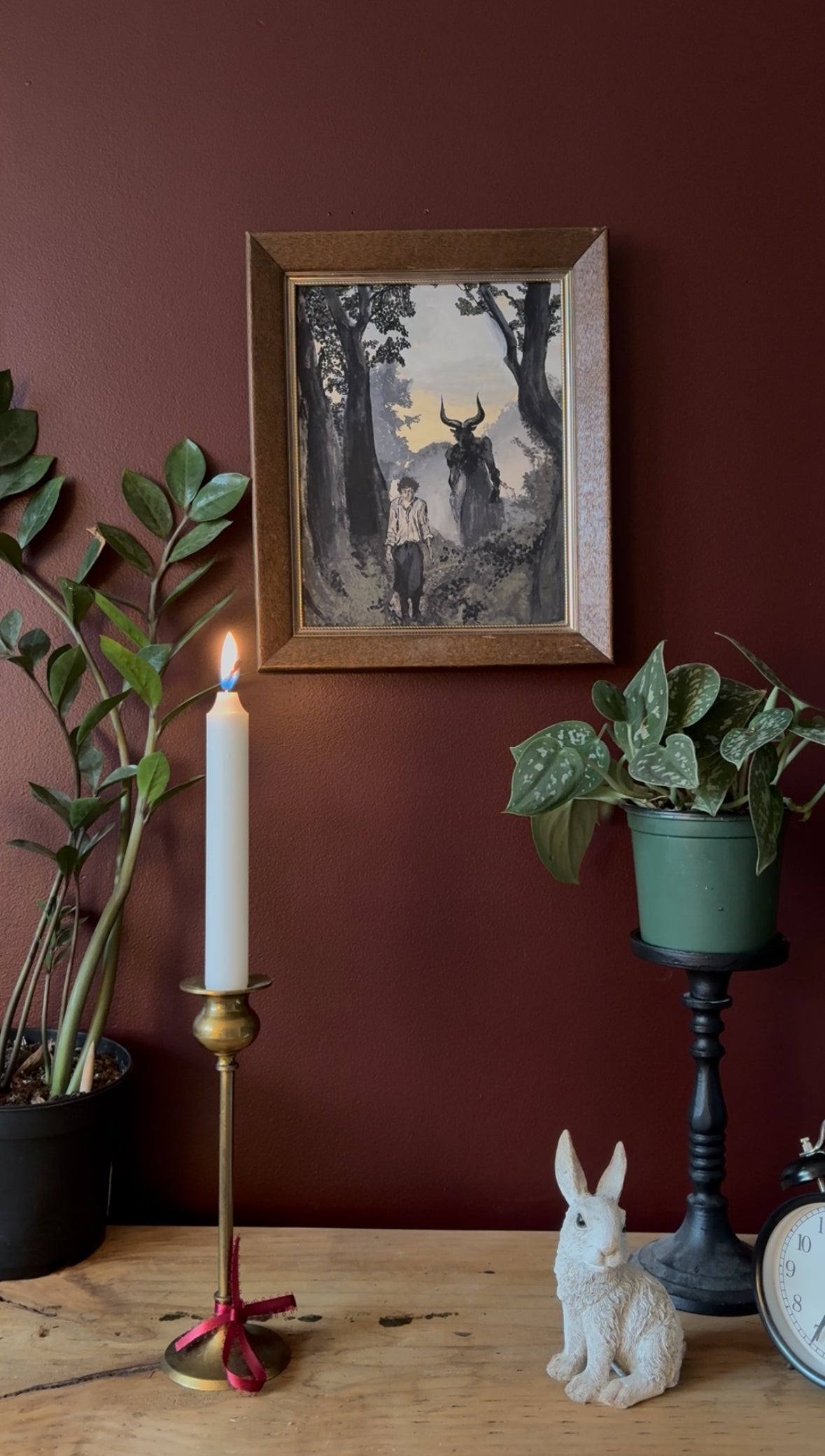 a fantasy inspired art print framed and hung against a red wall surrounded by plants