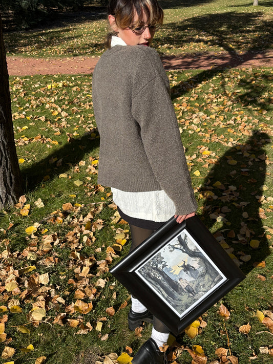 Person holding a framed art print by Laura Alexander outdoors on a grassy area with fallen leaves.