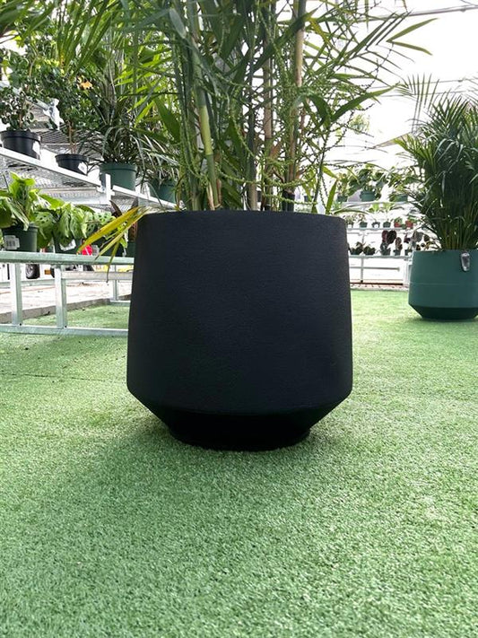 large matte black planter with plant inside in greenhouse