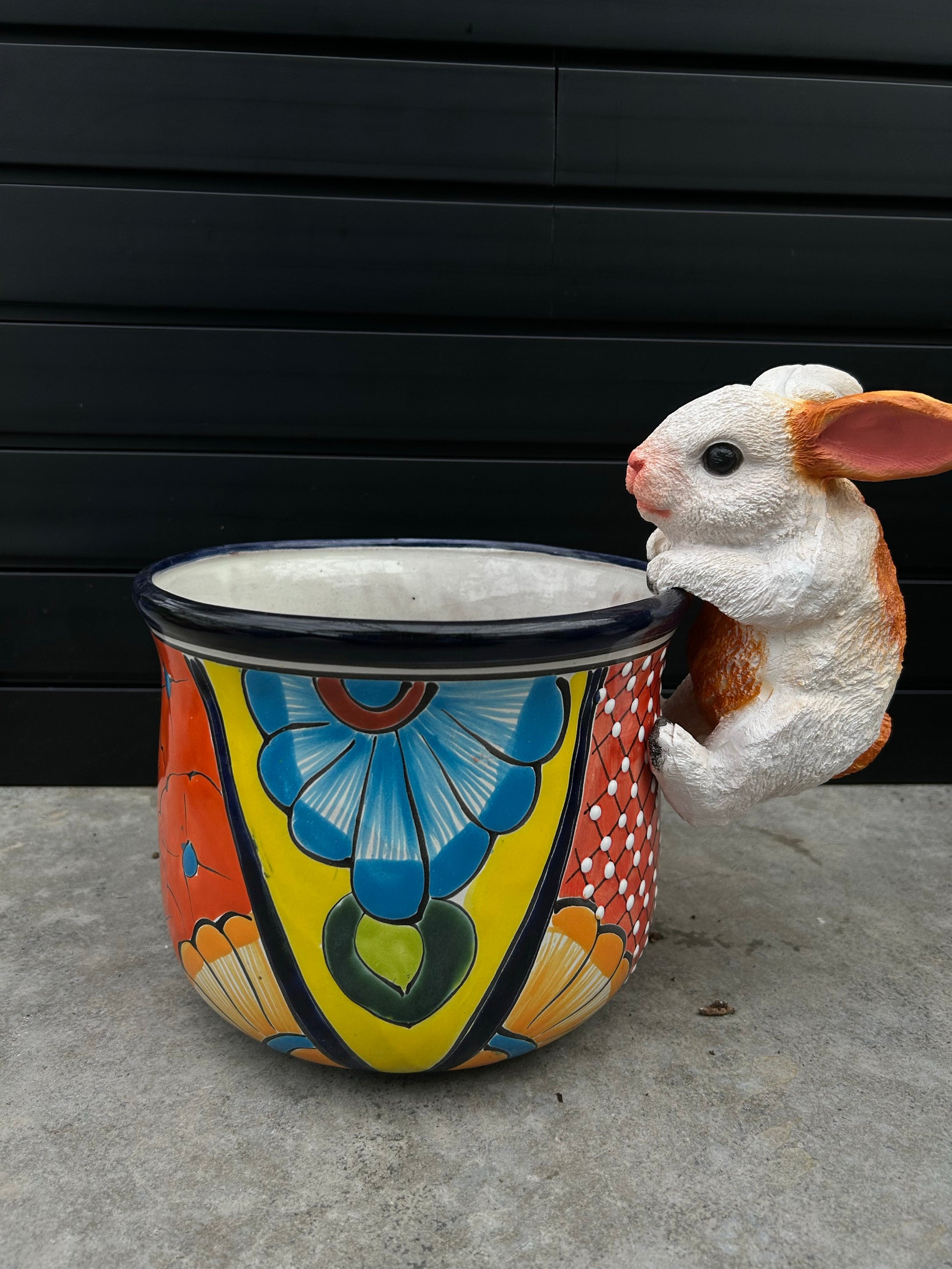 a brightly coloured and patterned ceramic pot with a ceramic bunny holding on to the lip