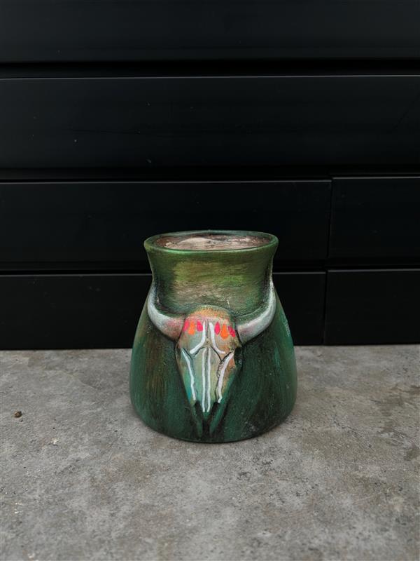 a small green ceramic planter with a bull skull design