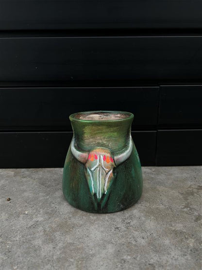a small green ceramic planter with a bull skull design