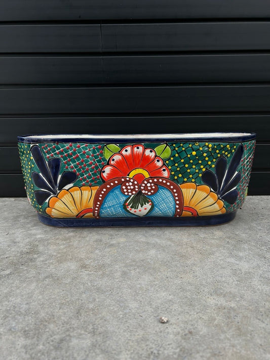 colourful canoe shaped planter resting on concrete floor with black slate background