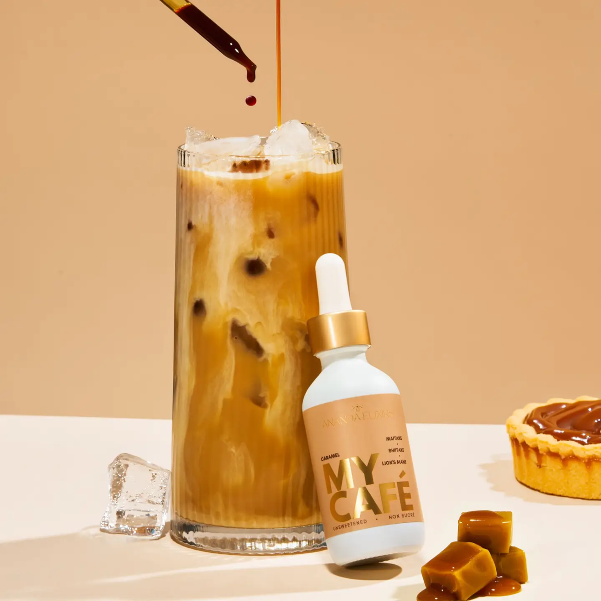 a white dropper bottle with a brown label that says my cafe caramel leaning against an ice coffee with a tan background