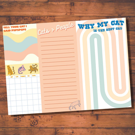 A notepad with a colorful cover featuring cat illustrations and the title 'Why My Cat Said PISSPS' at the top. Beneath the title are subheadings such as 'TELL ME ABOUT YOUR DAY' and 'WHY MY CAT IS THE BEST'.