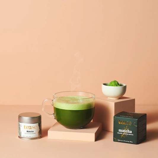 a clear mug of steaming ceremonial match next to its original tease packaging against a peach coloured background