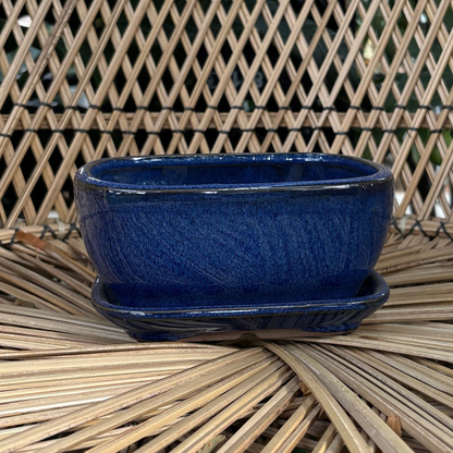 a small blue glossy rectangle shaped Chinese ceramic pot with a drip tray resting on a wicker chair