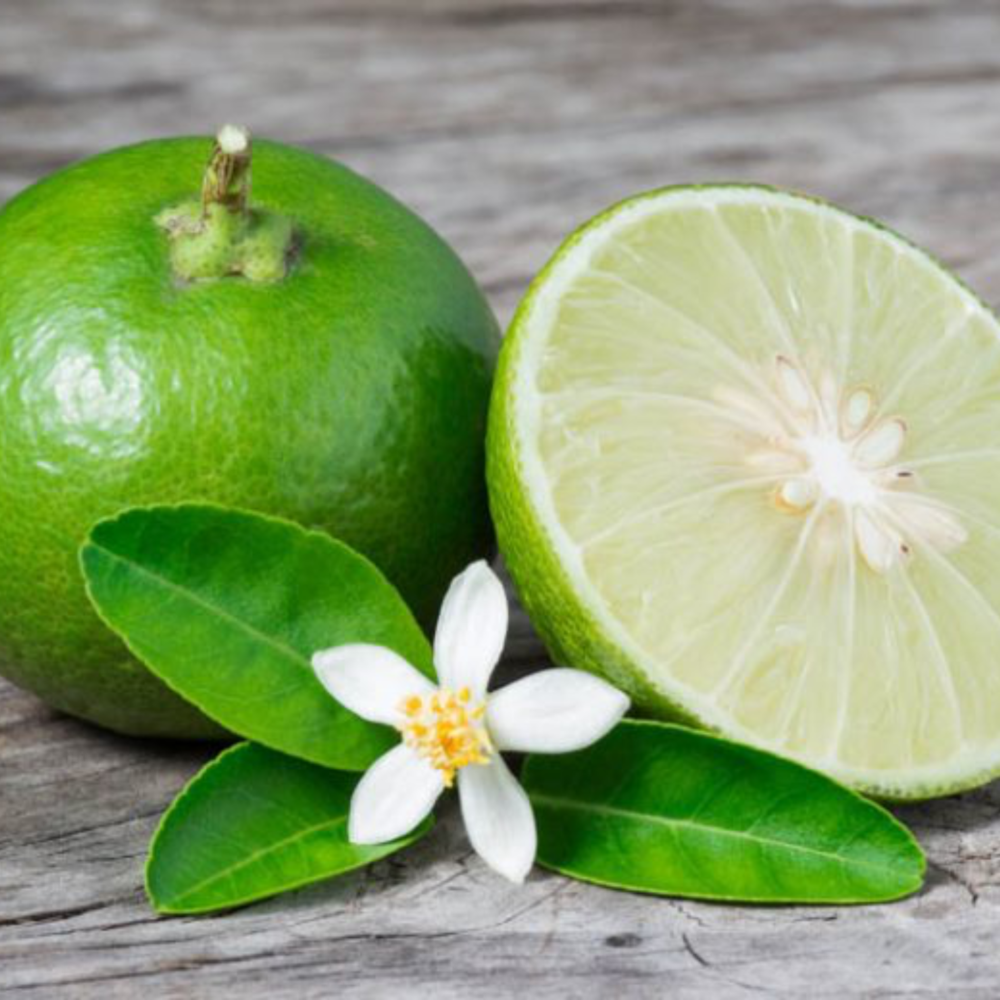 two limes one full and one half next to w white flower on a wooden surface