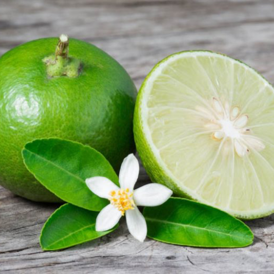 two limes one full and one half next to w white flower on a wooden surface