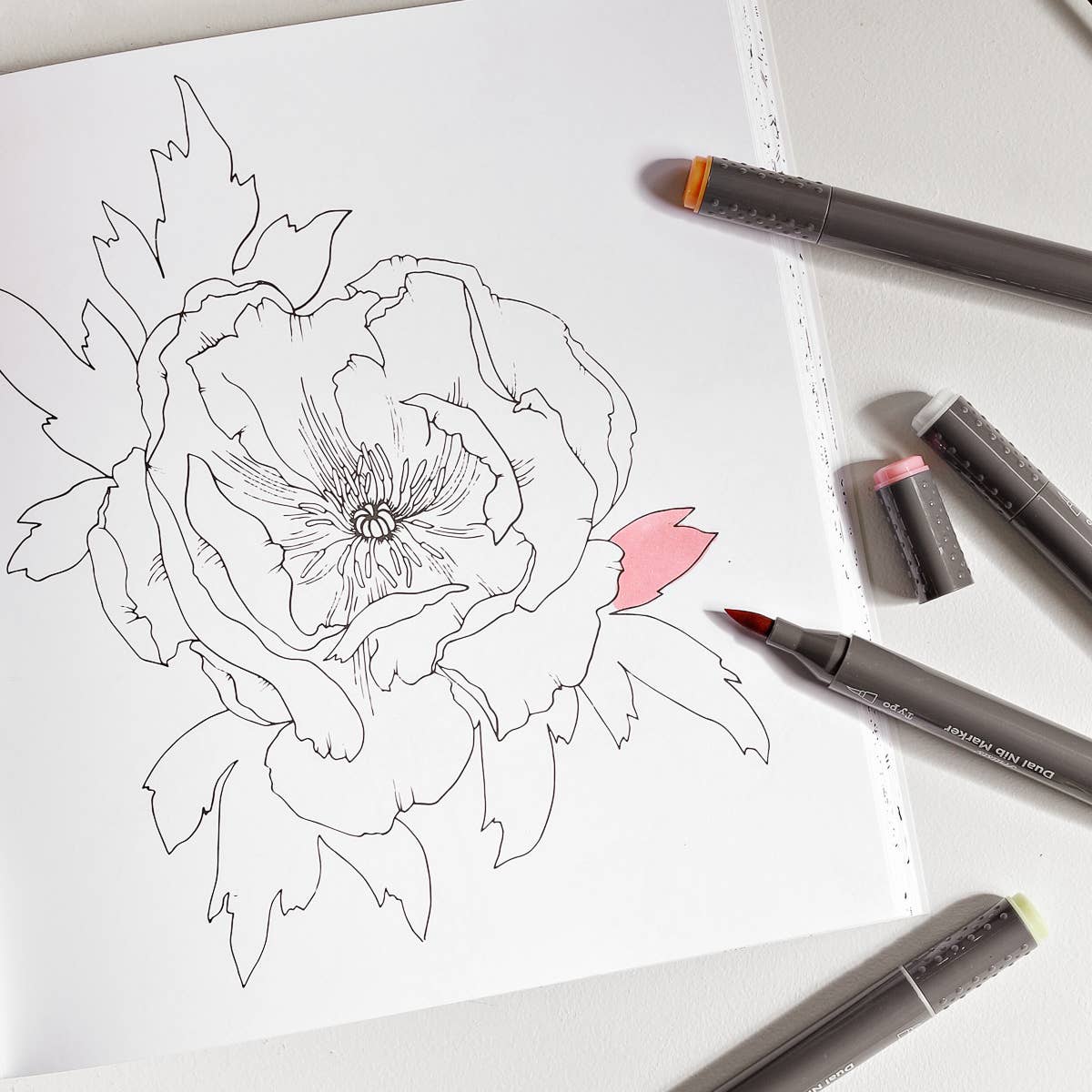 an open floral colouring page with markers spread across the page