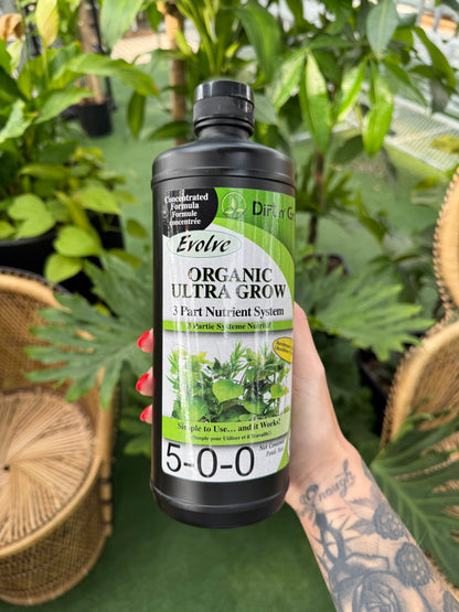 Hand holding a bottle of Evolve Organic Ultra Grow plant nutrient system against a green leafy background.