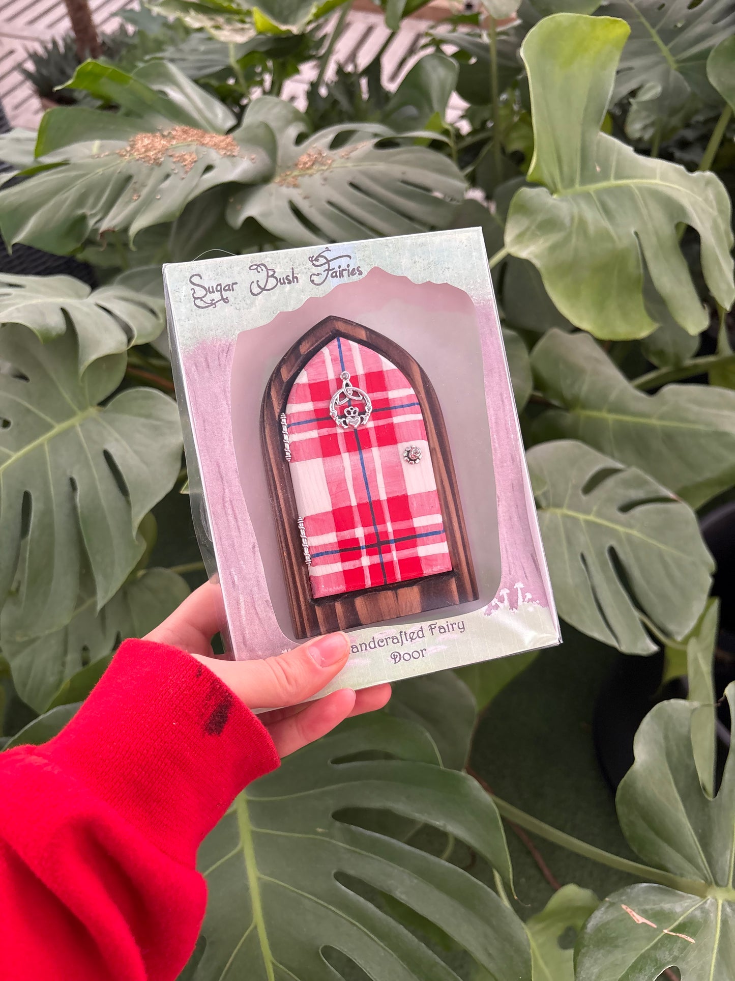 hand holding a red gingham patterned fairy door against a plant background