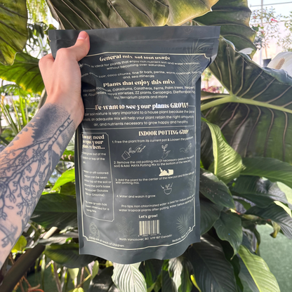 a person holding a dark green bag of Maya growing medium with back of the package being displayed showing the ingredients and use instructions of the product with many tropical plants in the background
