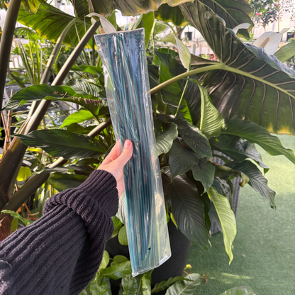 a person holding a plastic package of dark green floral and orchid mini stakes with many tropical plants in the background