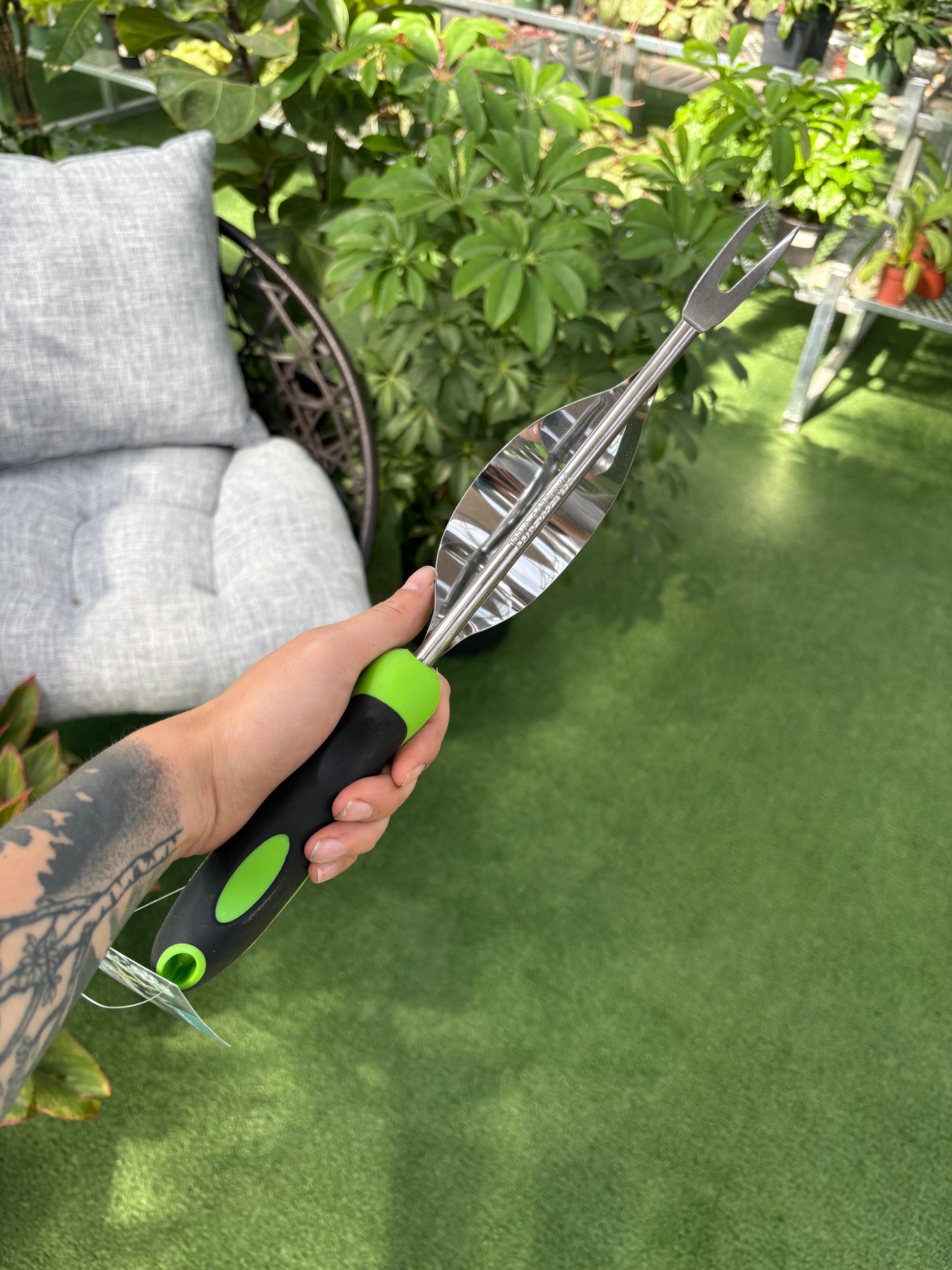 Hand holding a garden tool with a green handle against a blurred green background