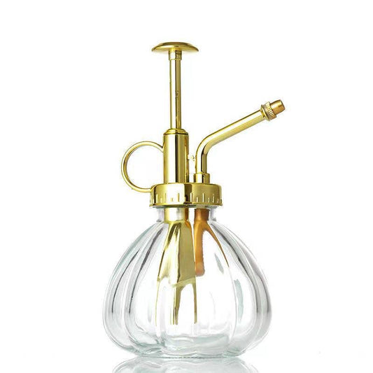 A stylish glass watering spray bottle with a gold-colored metal pump and spout.