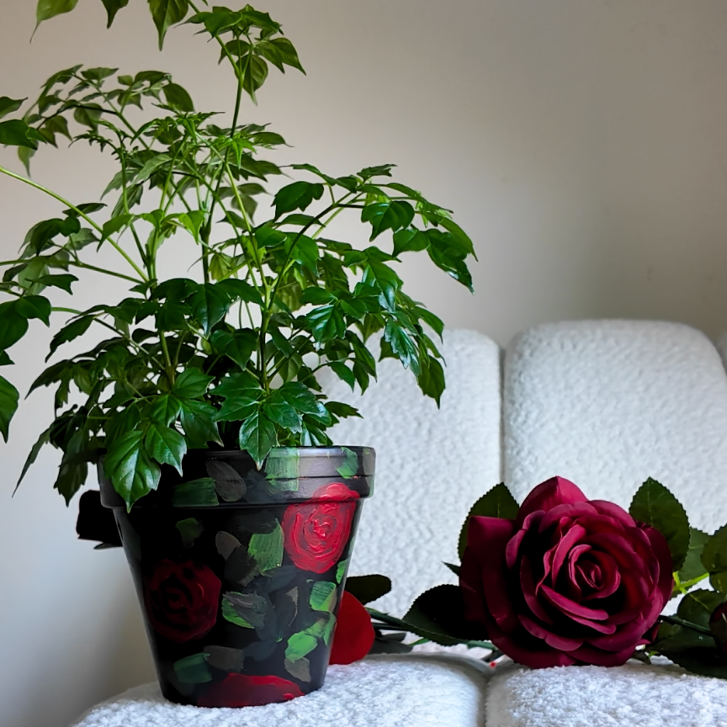 Potted plant with a decorative hand painted red roses pot with a red rose sitting next to it with a white background 