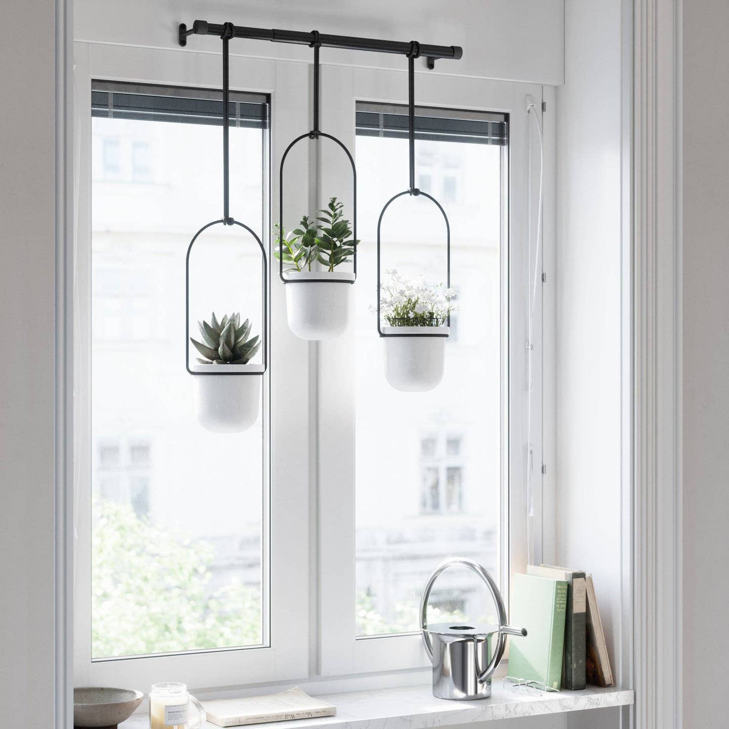 three white hanging planters attached to a black rod inform of a bright window