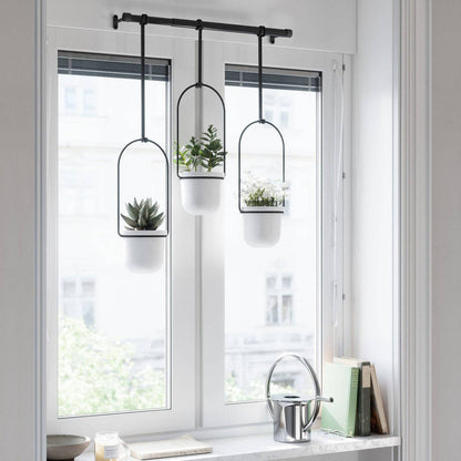 three white hanging planters attached to a black rod inform of a bright window
