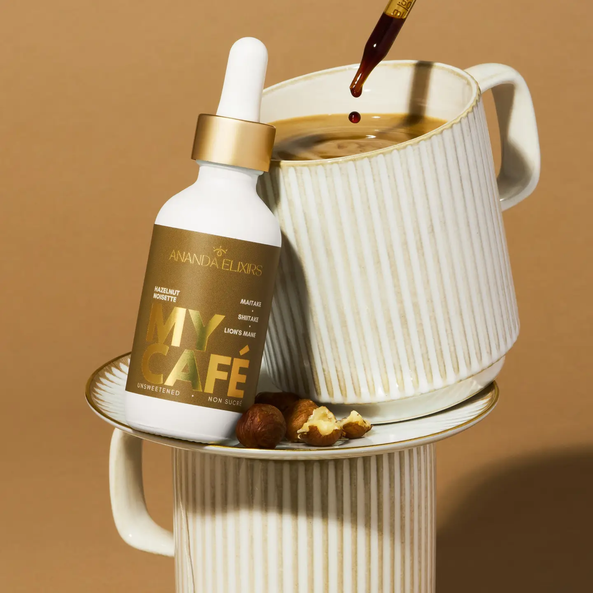 a white dropper bottle wth a brown label that reads my cafe hazelnut leaning against a white mug filled with coffee with a tan background