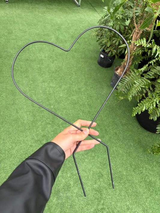 a person holding a black heart trellis for plants against green background