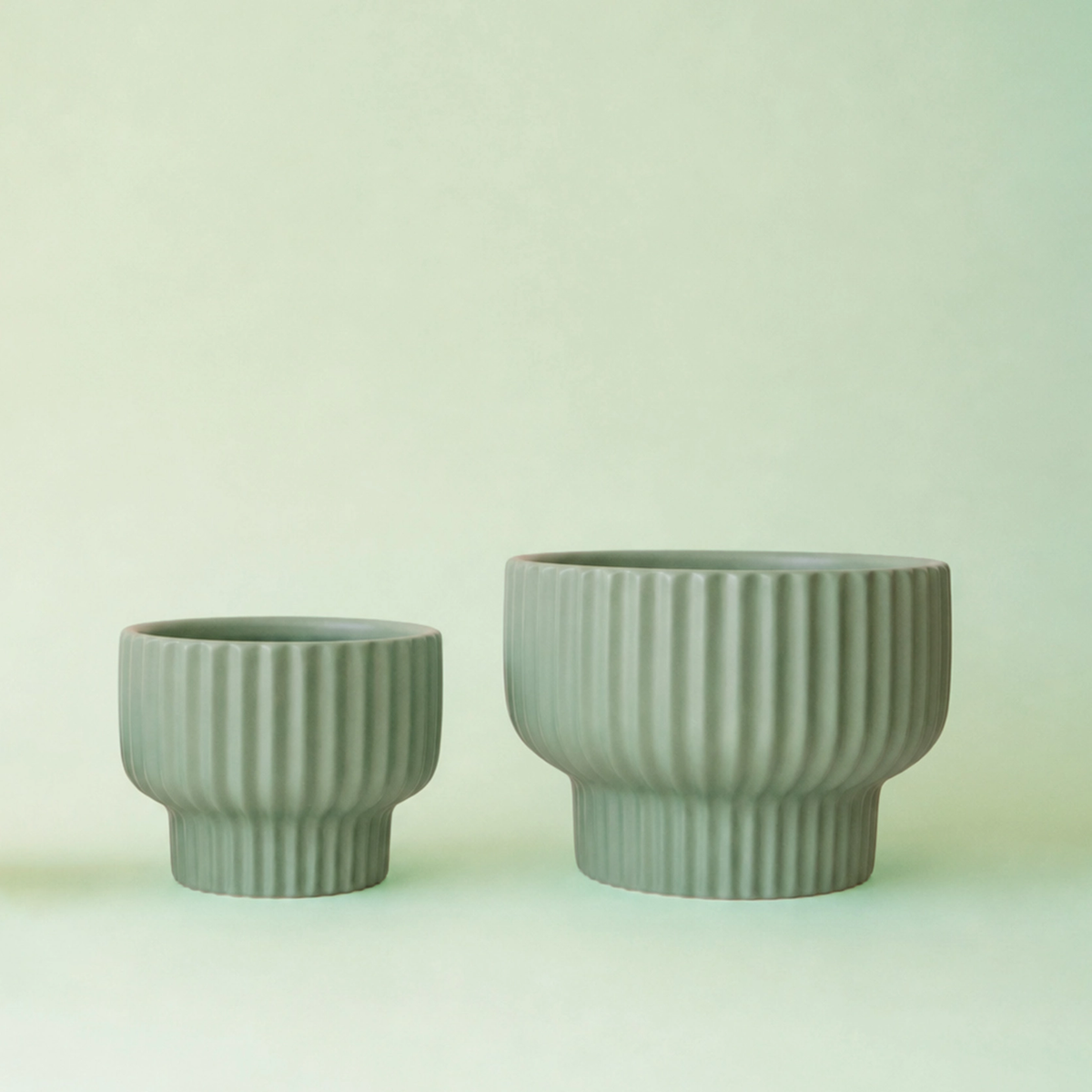 two jade coloured Presley pedestal planters of different sizes resting against a jade toned background